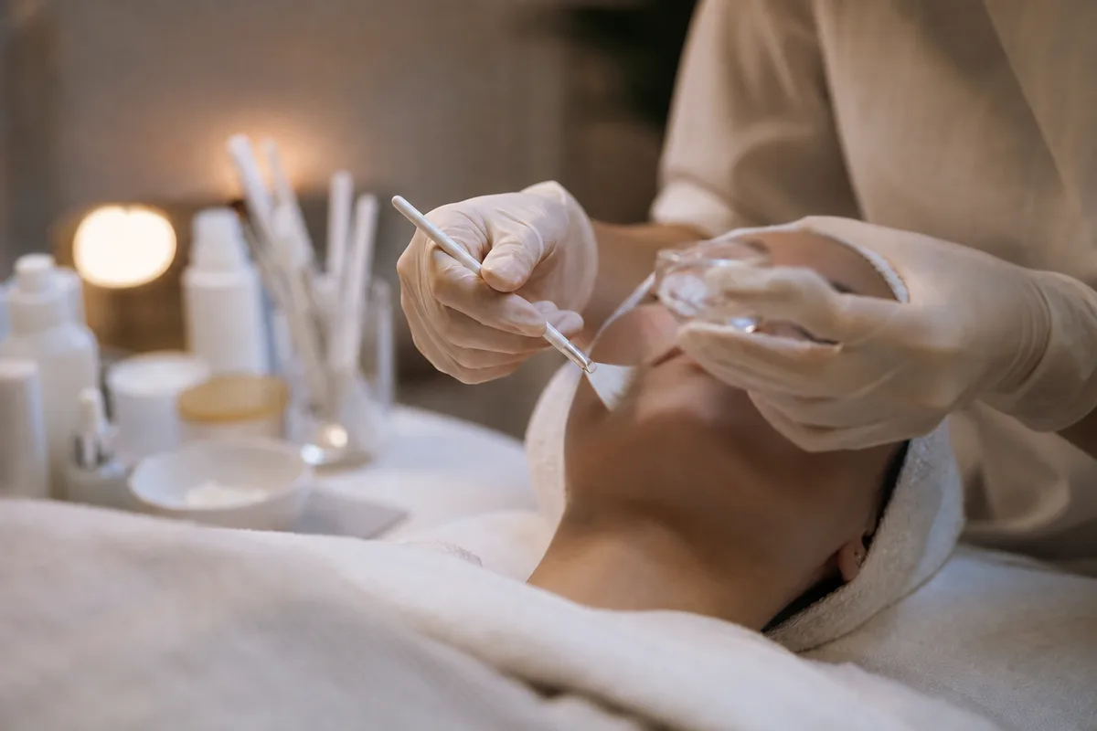 Mains gantées d’une esthéticienne réalisant un soin du visage en cabine