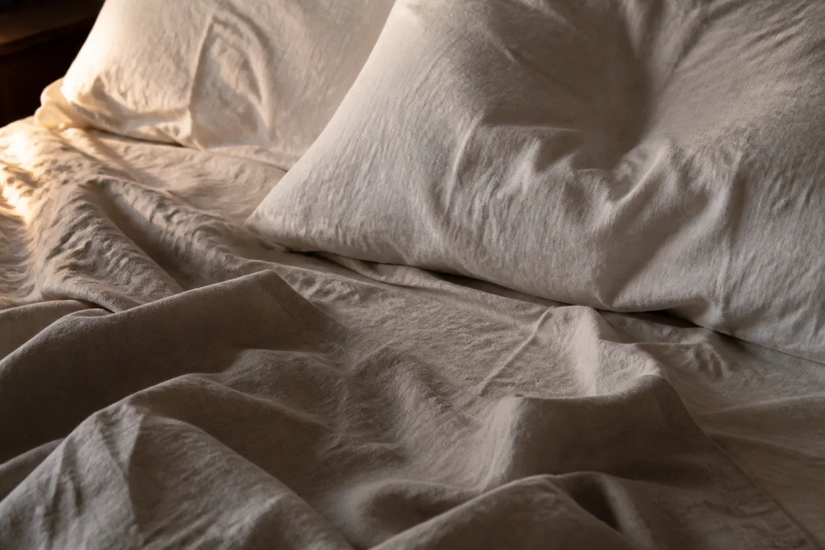 Draps de lin froissés sur un lit dans une lumière basse de fin de soirée